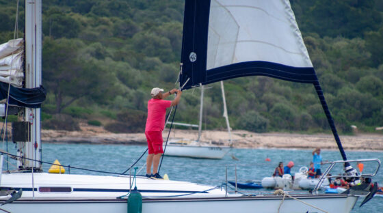 Man on a sailboat deck adjusting a furling sail