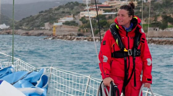 Woman standing on a sailboat deck in red foul weather gear with a Team O PFD - Rethinking PFDs