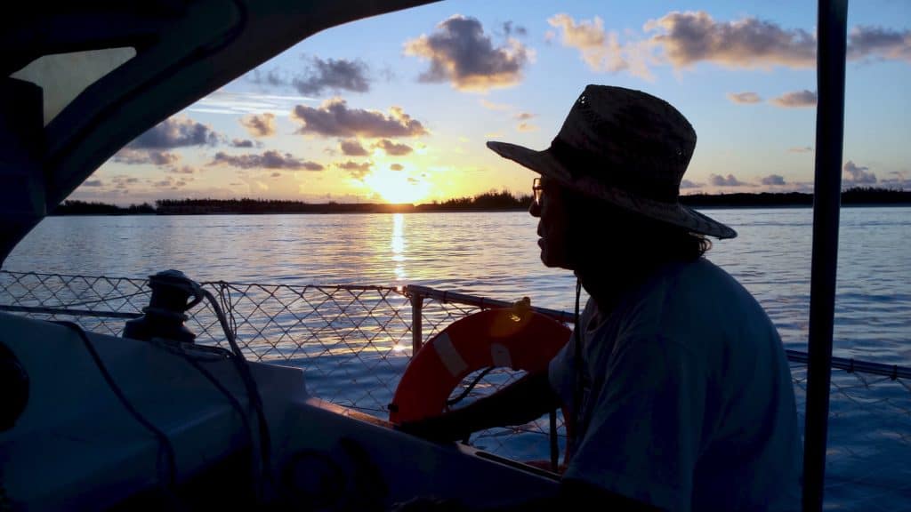 Silhouette of man in hat at anchor during sunset.