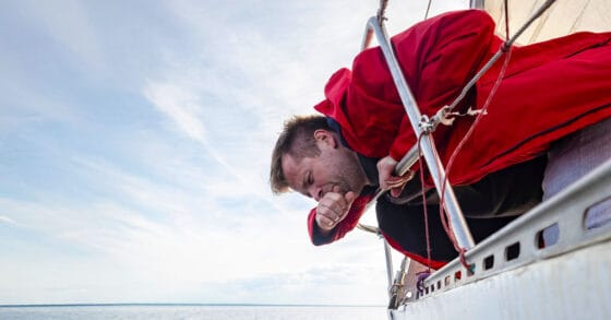 Man getting sick over the water from a sailboat - seasickness