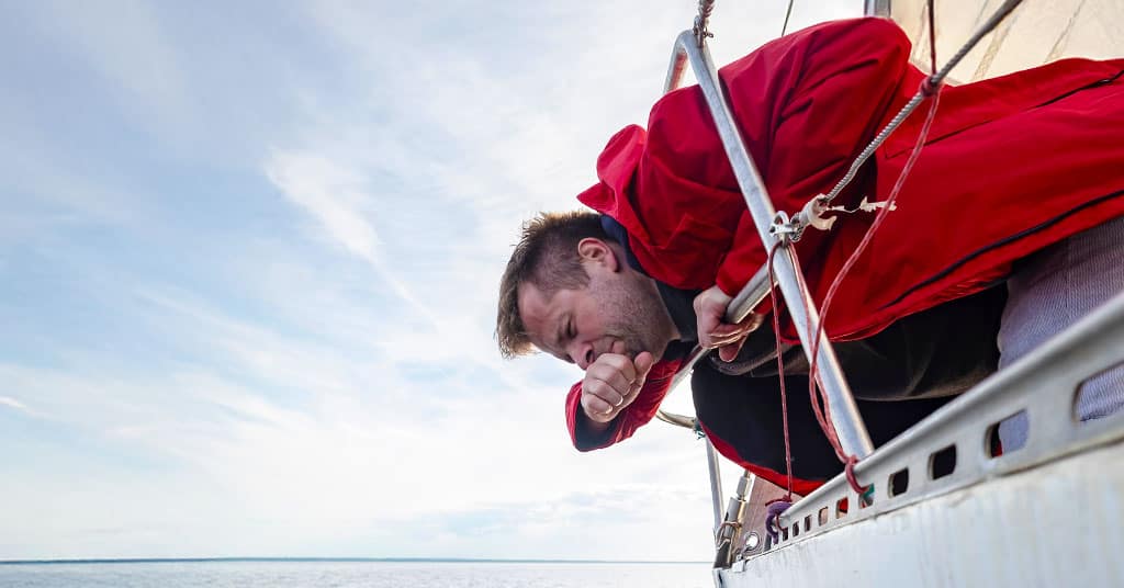 Man getting sick over the water from a sailboat - seasickness