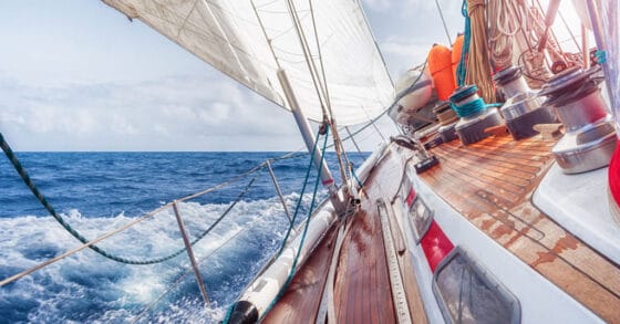 Boat with teak decks moving through the water - start living on a boat and cruising