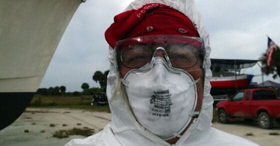 Person wearing white coveralls and a red hat with safety glasses and a dusk mask - dirty boat projects