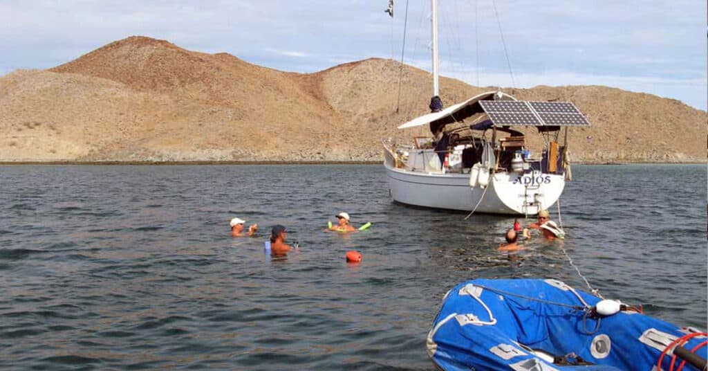 People swimming beside an anchored sailboat with mountains in the background - enjoy happy hour off your boat