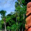 Dark red stone figure against a back drop of palm trees - long stay visa for French Polynesia