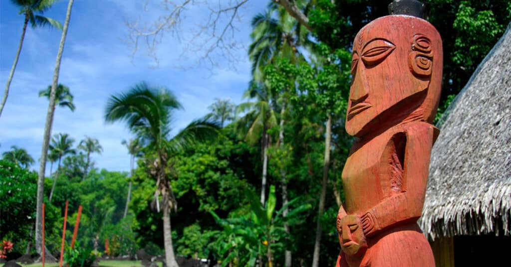 Dark red stone figure against a back drop of palm trees - long stay visa for French Polynesia
