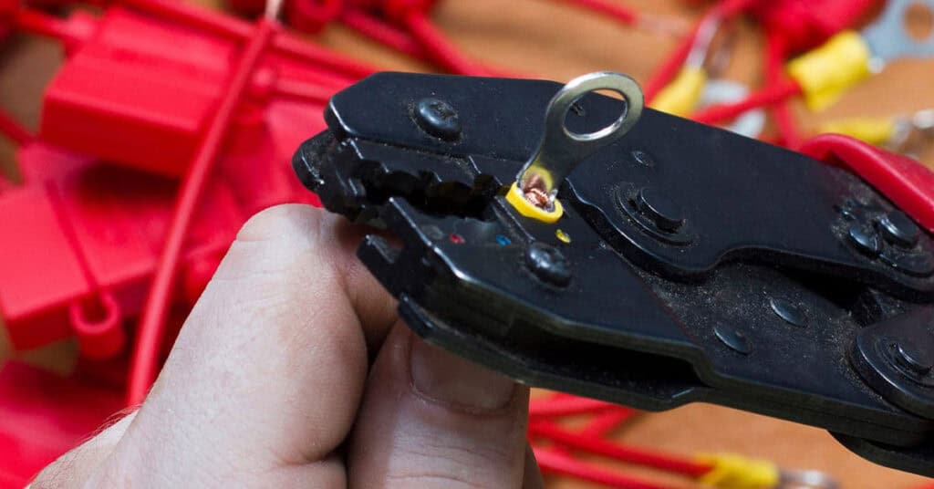 Hand holding a crimping tool and a wire - Tips for Boat Wiring