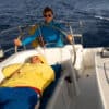 Person lying on boat while another stands at the wheel - when a crew members gets sick