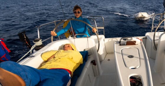 Person lying on boat while another stands at the wheel - when a crew members gets sick