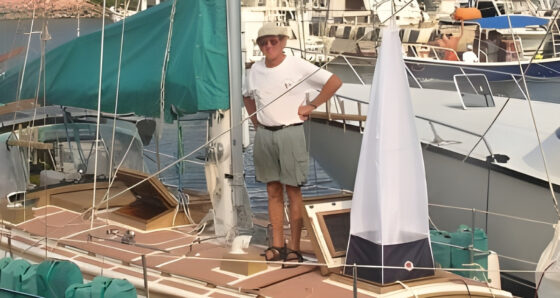 Sailor standing on sailboat deck with a white 4-way wind scoop set in a forward hatch