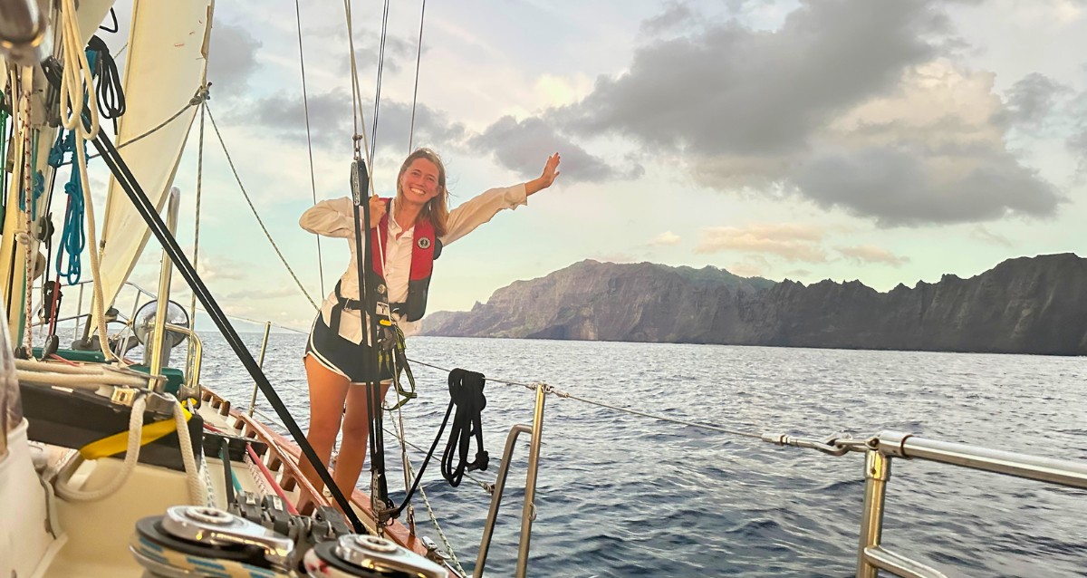 Cruiser celebrating on deck with arms outstretched, dramatic coastline in background — navigating the first-year learning curve