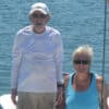 An older couple smiling on their sailboat, showing that sailing in your 70s is very much possible.