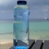 bottle of water on the shore with sailboat in the background - do you need a watermaker