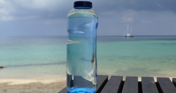 bottle of water on the shore with sailboat in the background - do you need a watermaker
