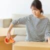 Woman taping a moving box while downsizing to live on a boat, packed boxes around her