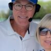 A man and woman wearing 2Talk Bluetooth marine intercom headsets — known as "Marriage Savers" — on a boat in a marina, both with behind-the-neck headbands and boom microphones positioned at their mouths.