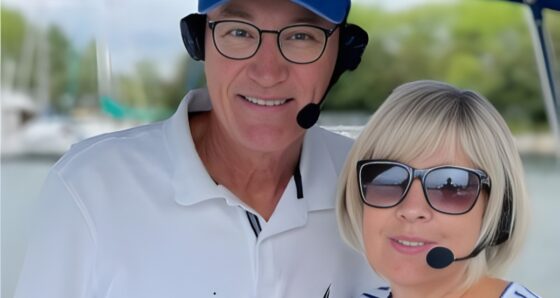 A man and woman wearing 2Talk Bluetooth marine intercom headsets — known as "Marriage Savers" — on a boat in a marina, both with behind-the-neck headbands and boom microphones positioned at their mouths.