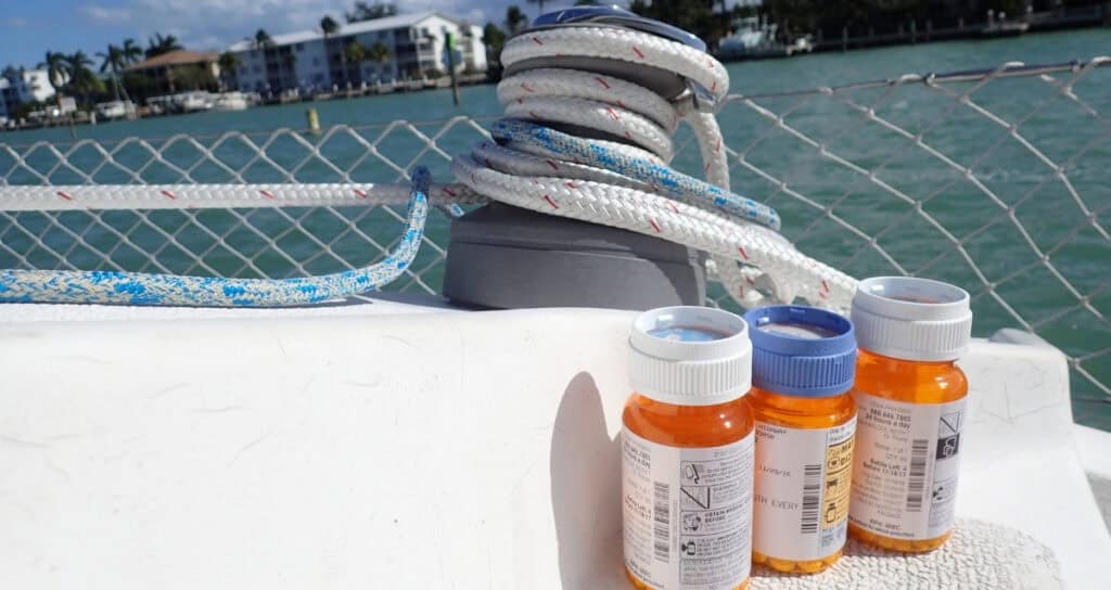 Three prescription medication bottles sitting on a sailboat deck with mooring lines and a marina in the background