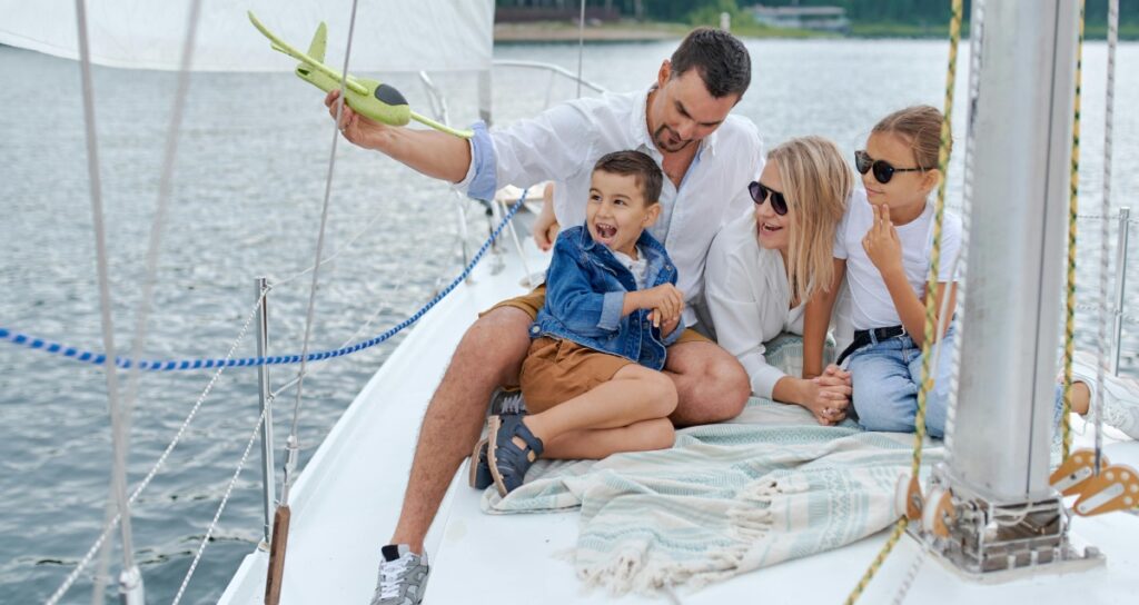 Man with airplane, boy, girl and woman on the bow of a sailboat - cruising with family