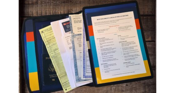 The Boat Galley Boat Documents Organizer open on a wooden table, showing a Florida vessel registration certificate, U.S. passport, insurance documents, and other boat paperwork tucked into the left side of the binder, with the printed Boat Documents Checklist for U.S. Boating displayed on the right side.