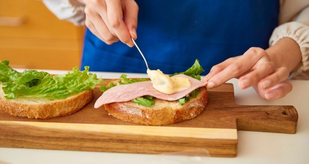 Spreading mayonnaise onto a sandwich with a clean spoon — the key rule for keeping mayo unrefrigerated