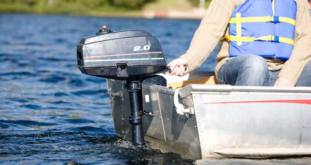 Person in life vest operating a small outboard motor on an aluminum boat