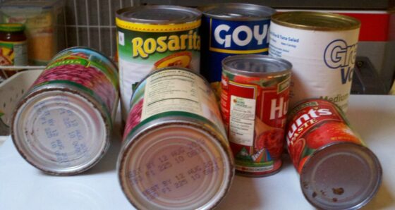 Several canned food brands on their sides showing rust on rims and lids