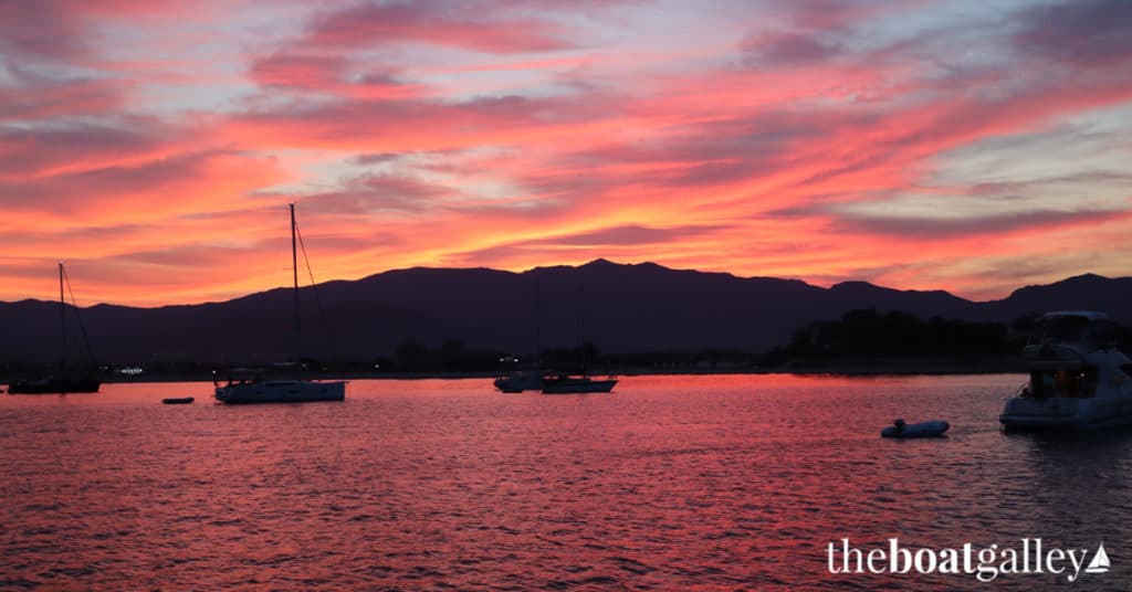 Sunset over a quiet anchorage with sailboats silhouetted against a warm sky