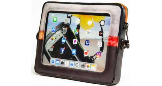 A brown and orange ugo Tablet XL waterproof tablet case with orange uZIP drysuit-style zipper, holding a 13" iPad displaying its home screen visible through the clear front of the case.